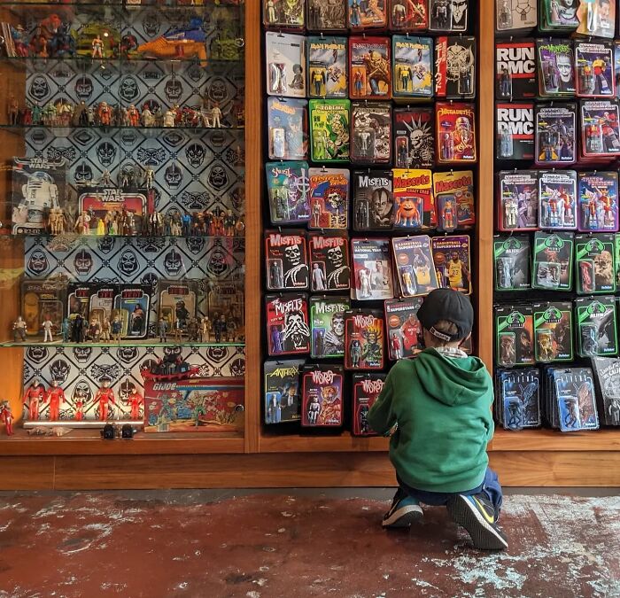 A child in a green hoodie admires an array of colorful toys in a San Francisco shop, as captured by photographer Akaboshi.