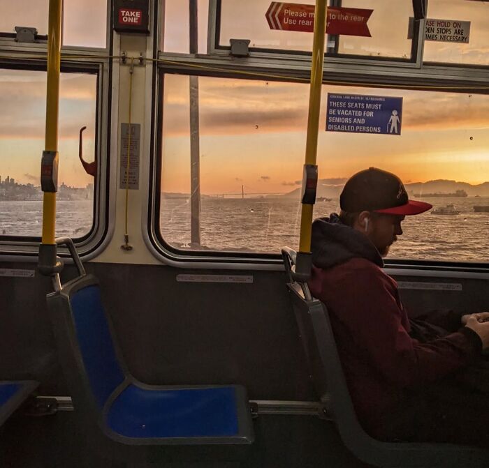 Man sitting in a San Francisco bus, viewing a coastal sunset through the window.