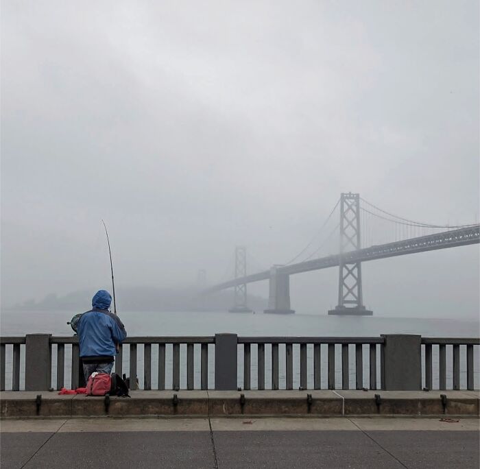 Person fishing by a foggy Golden Gate Bridge in San Francisco.