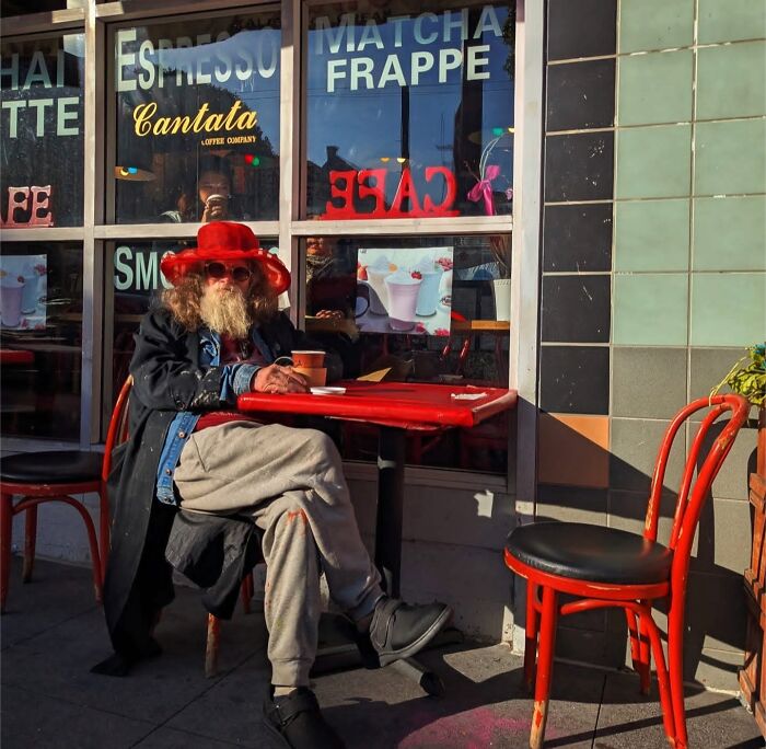 San Francisco street scene with a person in a red hat and coat sitting outside a café, captured by photographer Sage Akaboshi.
