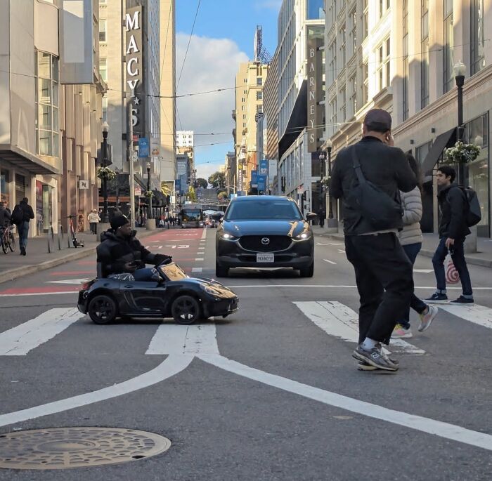 San Francisco street scene with pedestrians and a child in a toy car, captured by photographer Sage Akaboshi.
