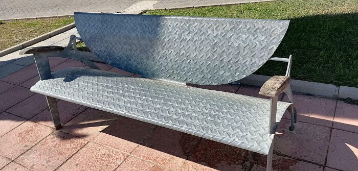 Bench design fail with a high, unusable backrest placed in a park setting.