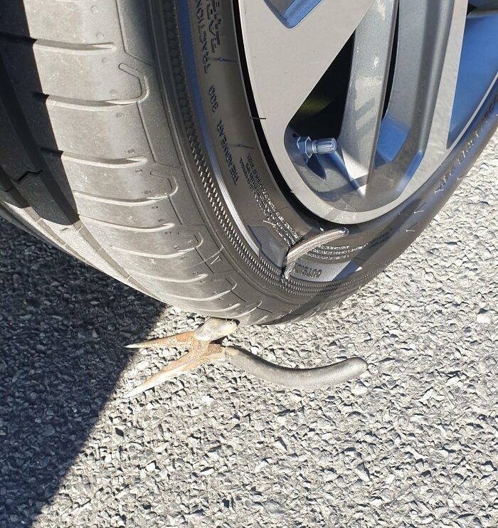 Car tire punctured by a metal hook on road, showing an expensive accident.