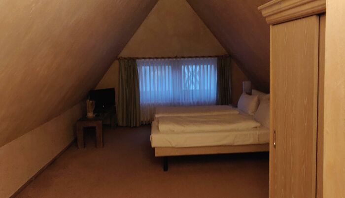 Cozy attic room with a bed, small table, and TV near a window with curtains.