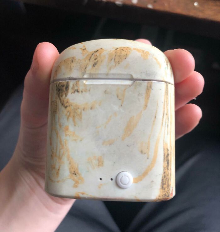 Hand holding marble-patterned earbud case with misaligned lid, illustrating a design fail.