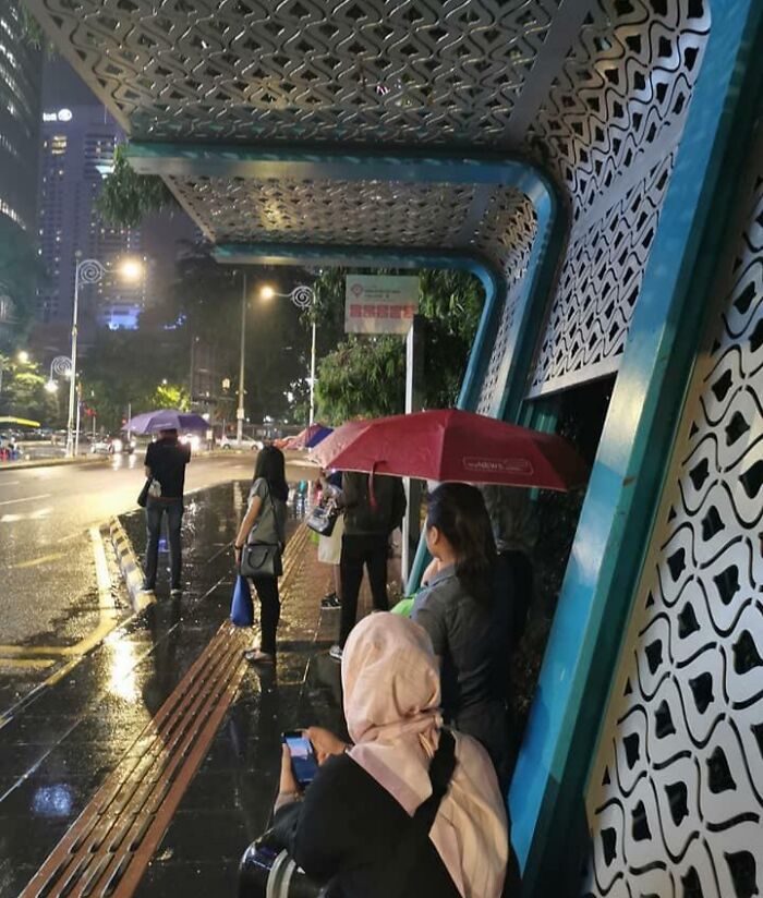 People under an ineffective shelter in the rain, highlighting a design fail in urban architecture.
