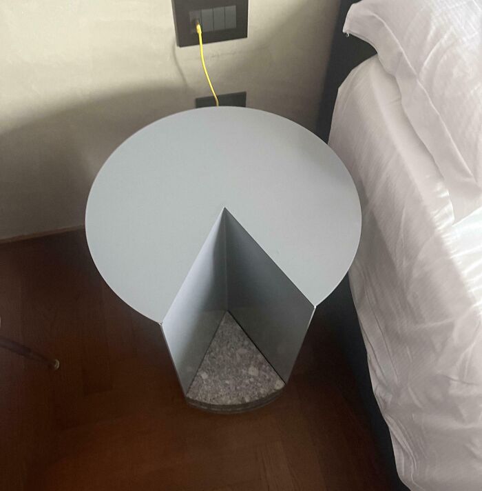 Unique design fail with a round side table missing a slice, beside a bed, illustrating design mishap.