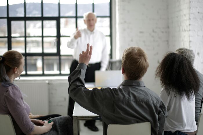 People in a casual meeting, one raising a hand, suggesting simple approaches for better life.