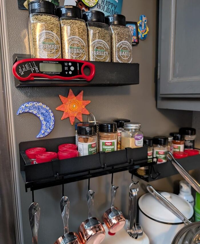 Kitchen game-changers: spice rack with jars of rosemary, oregano, parsley, and basil, plus hanging measuring spoons.