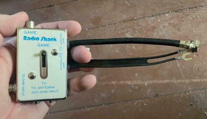 Vintage 1980s Radio Shack TV switch box held in a hand on a wooden floor background.