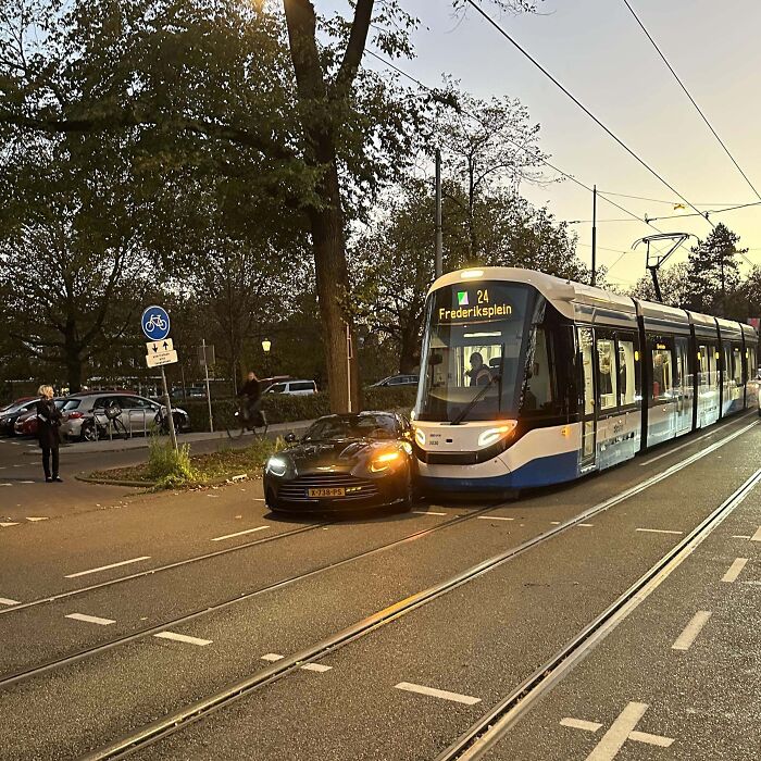 Tram collides with luxury car on tracks during sunset; costly accident scene.