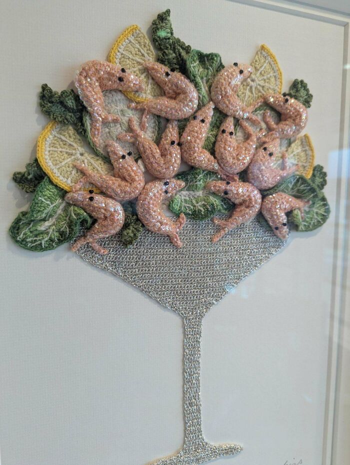 Crochet artwork of a shrimp cocktail in a glass with lemon wedges and leafy greens, showcasing incredible crochet skills.