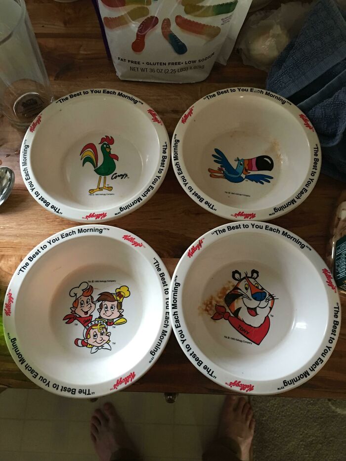 1980s cereal bowls featuring cartoon characters like Corny the Rooster and Tony the Tiger on a wooden table.