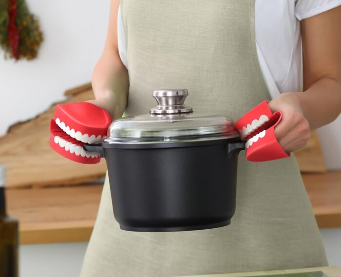 Person holding a pot with red novelty pot holders shaped like teeth, highlighting a kitchen game-changer.
