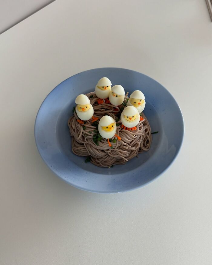 Adorable food art scene with boiled egg chicks on a noodle nest by a Korean artist in a blue bowl.