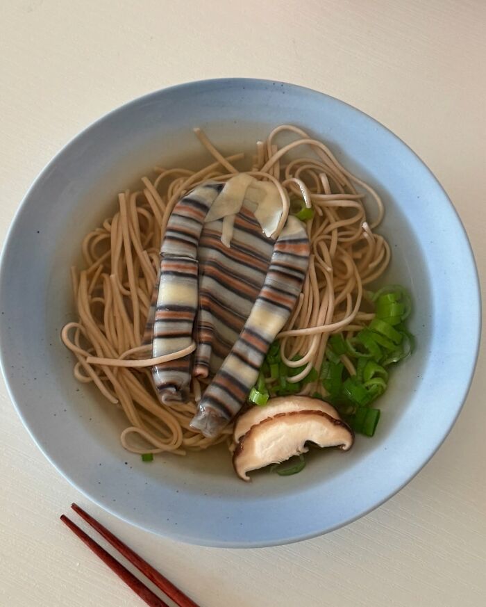 Adorable food art arrangement featuring noodles, green onions, and a mushroom slice in a bowl.