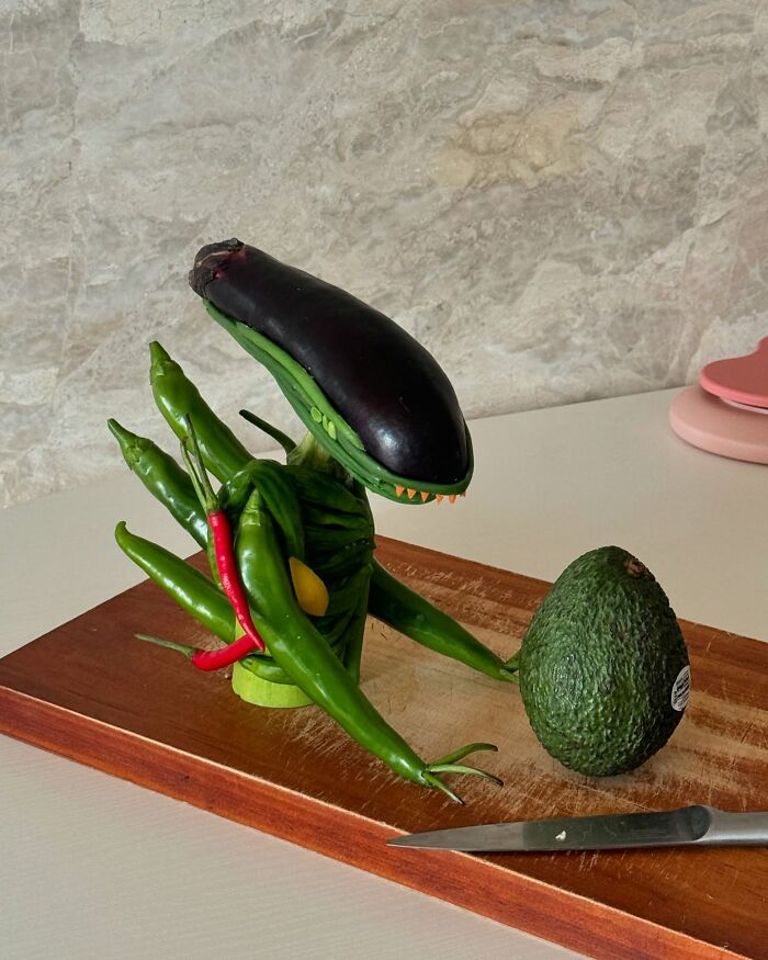 Korean artist's adorable food art featuring a creature made of vegetables next to an avocado and knife on a wooden board.