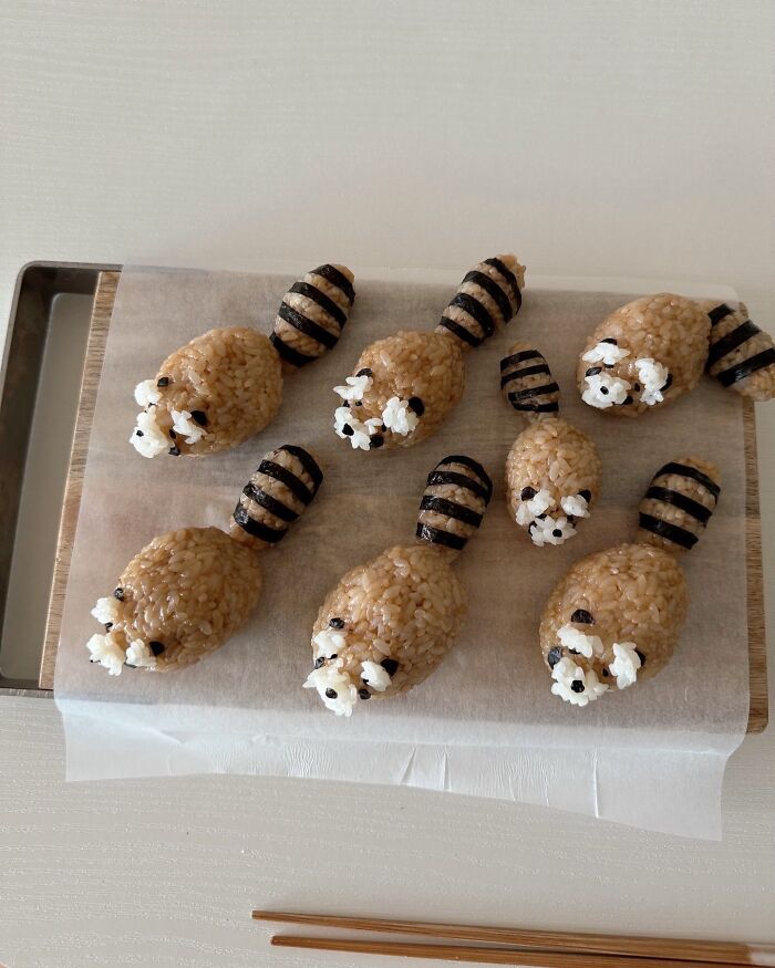 Korean artist's adorable food art featuring rice shaped like cute animals on a parchment-lined tray, with chopsticks nearby.