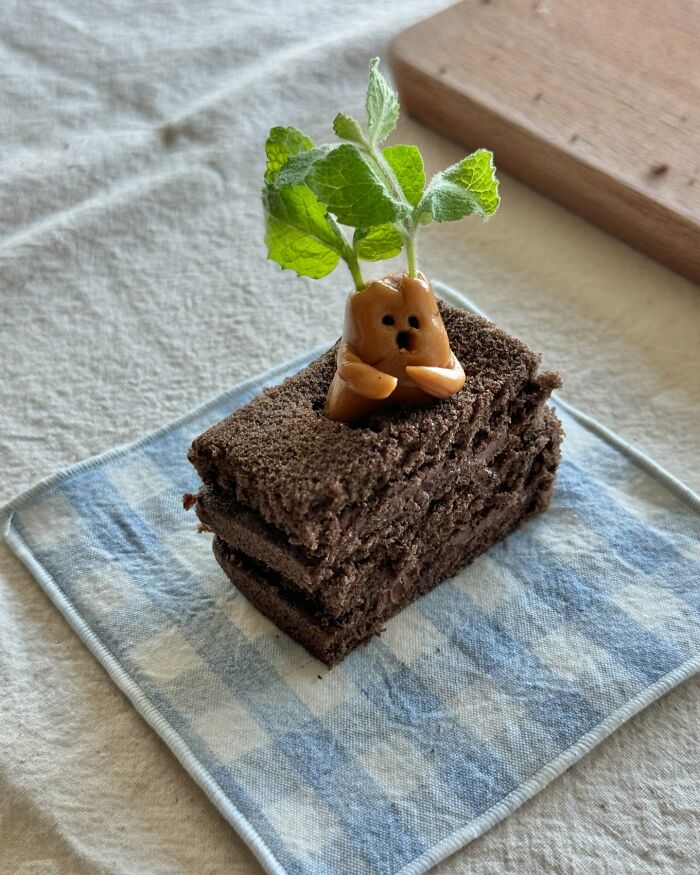 Adorable food art with chocolate cake shaped like a cute creature, garnished with mint leaves on a checkered cloth.