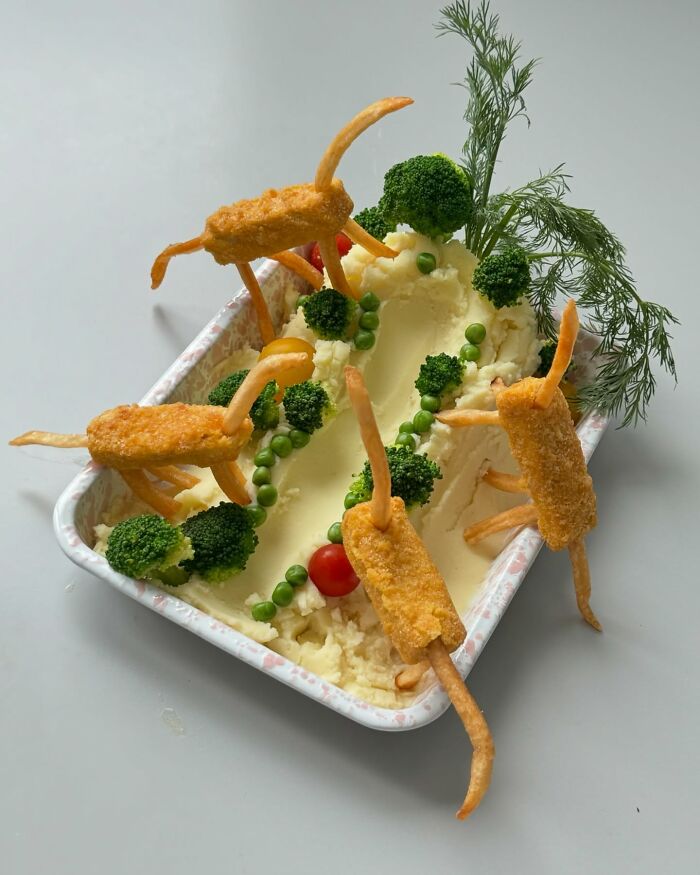 Adorable food art featuring fried items as animals on a creamy mashed potato landscape with broccoli trees and a tomato.