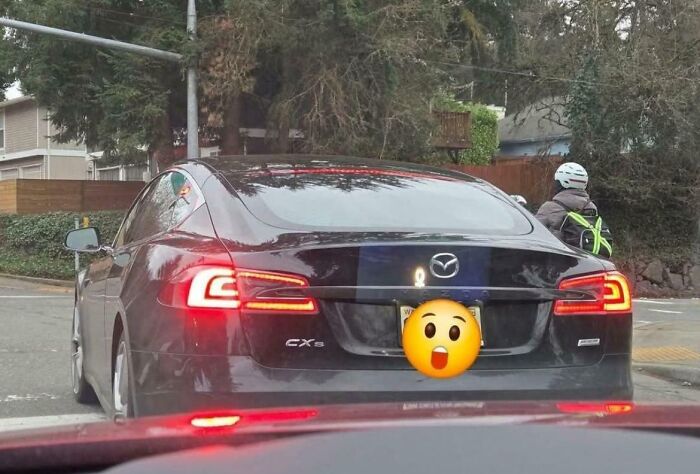 Mazda CX-5 at a traffic light with a humorous emoji covering the license plate, depicting an attempt at privacy.