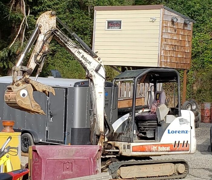 Excavator with a playful eye decal and a trailer, capturing an amusing Amazon masterpiece moment outdoors.
