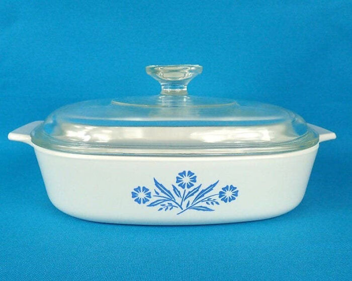 1980s vintage casserole dish with floral design, clear glass lid, and blue background.