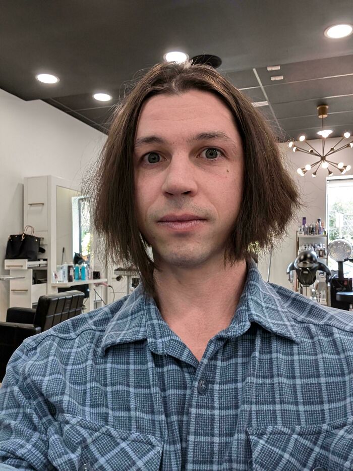 Man with an unfortunate haircut, long shaggy brown hair, looking at the camera in a salon.