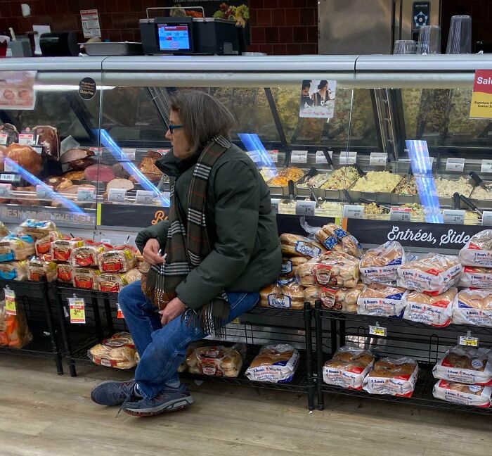 Person sitting on bread shelf in grocery store, displaying customer cluelessness.