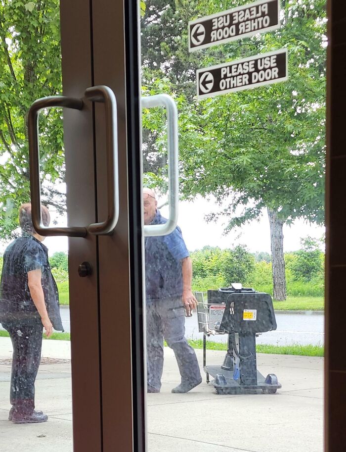 Two people stand outside a door marked "Please Use Other Door," embodying customer cluelessness.