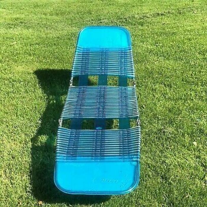 Blue 1980s lawn chair on green grass, showcasing retro design vibes.