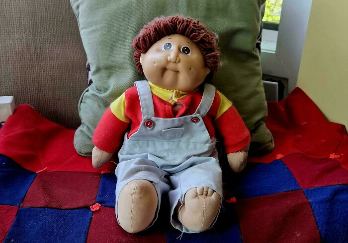 1980s doll with curly hair and overalls sitting on a colorful quilt, capturing the nostalgic vibe of the decade.