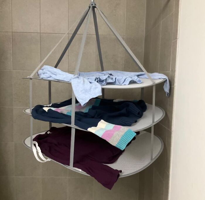 Clothes drying on a three-tier hanging rack for improved quality of life in a tiled room.
