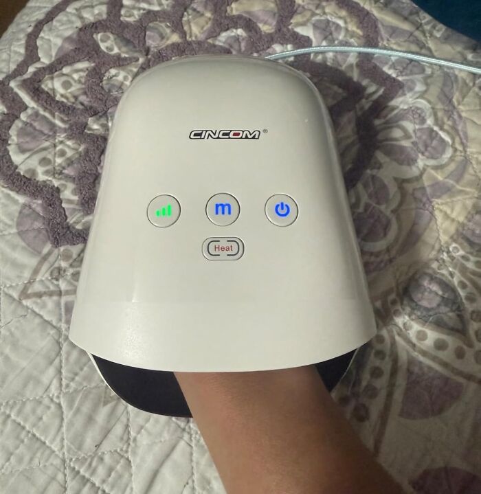 Hand inside a CINCOM massager on a patterned bedspread, enhancing quality of life with comfort features.