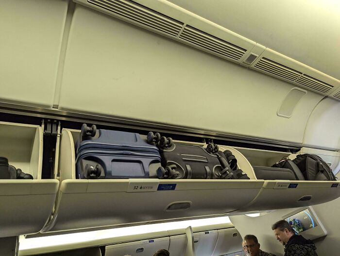 Airline baggage fail with improperly closed overhead bin and luggage protruding, causing inconvenience.