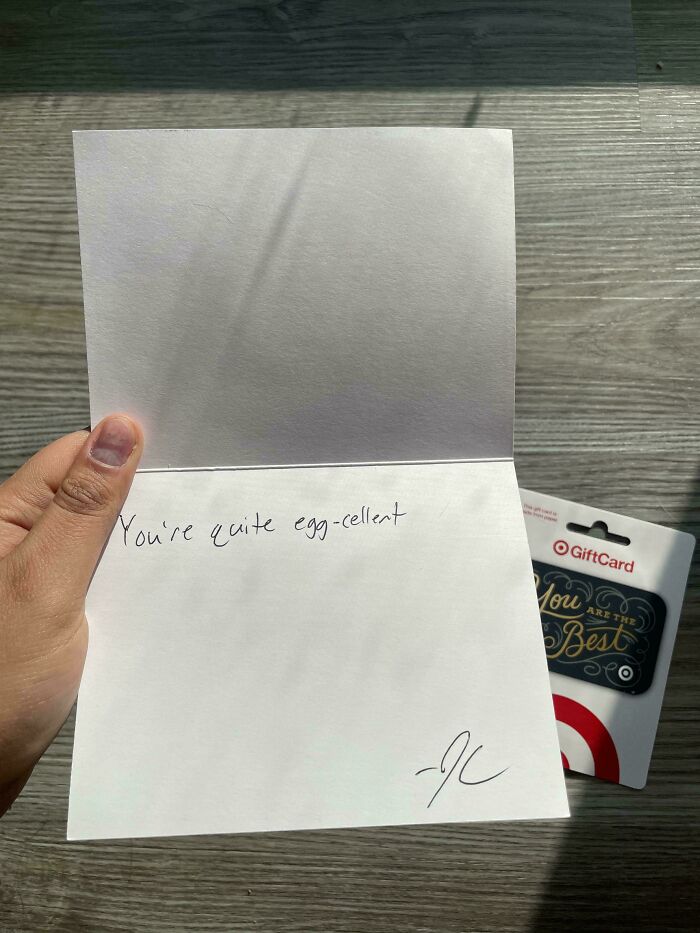 Hand holding a card saying "You're quite egg-cellent" with a gift card in the background, capturing a tough day at work.