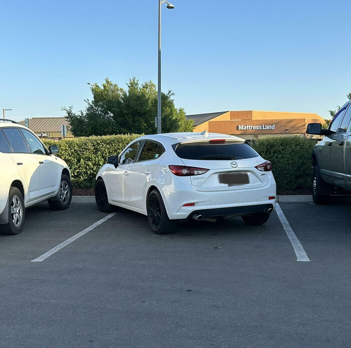White car parked poorly across two spaces in a parking lot, showcasing customer cluelessness.