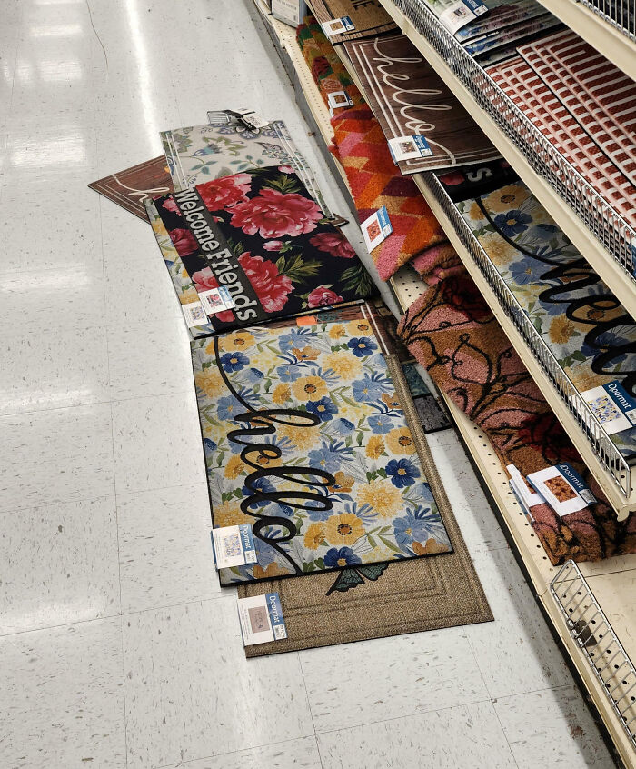 Store aisle with welcome mats stacked, showcasing customer cluelessness in product arrangement.