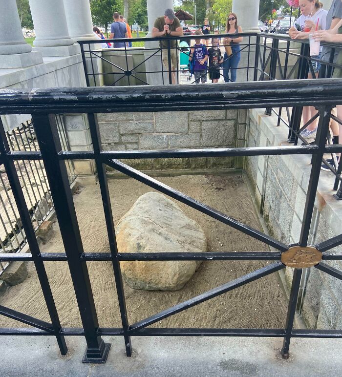 Awe-inspiring photo of an iconic place, featuring a historical rock monument enclosed by a metal fence with visitors nearby.