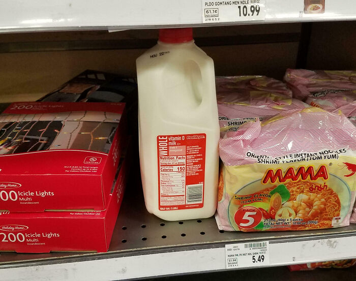 Milk misplaced on a store shelf between icicle lights and ramen, highlighting customer cluelessness.