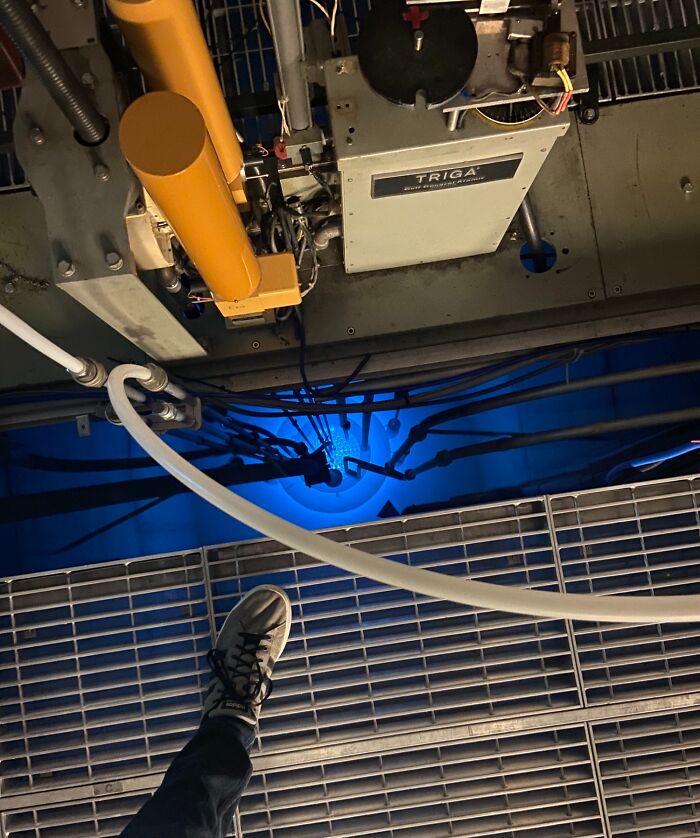 A foot on a metal grate overlooking a TRIGA reactor core emitting blue light, showcasing iconic nuclear technology.