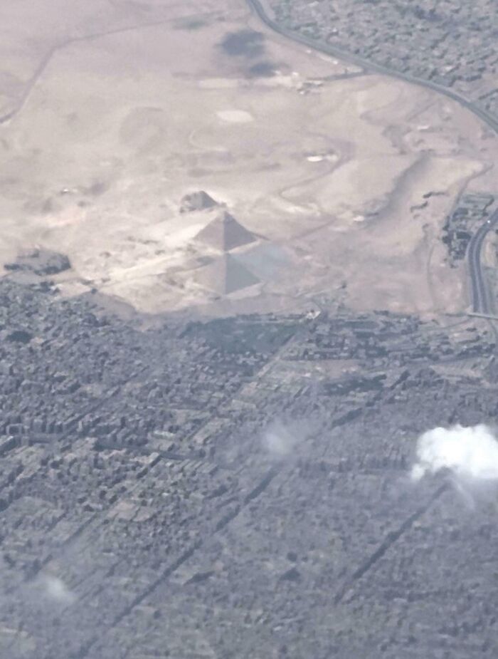Aerial view of iconic Pyramids of Giza in a desert landscape next to urban development, Egypt.