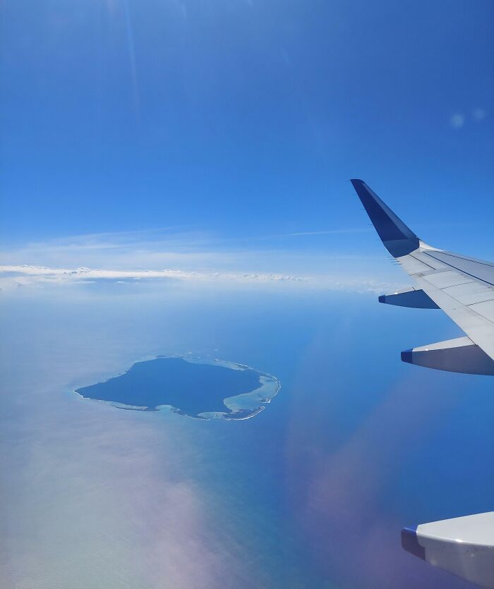 Airplane wing view of an iconic island surrounded by blue ocean under a clear sky.