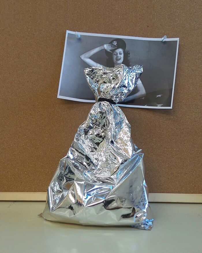 Tin foil shaped like a dress under a photo of a saluting woman, illustrating the art of illusion in clever fusions.