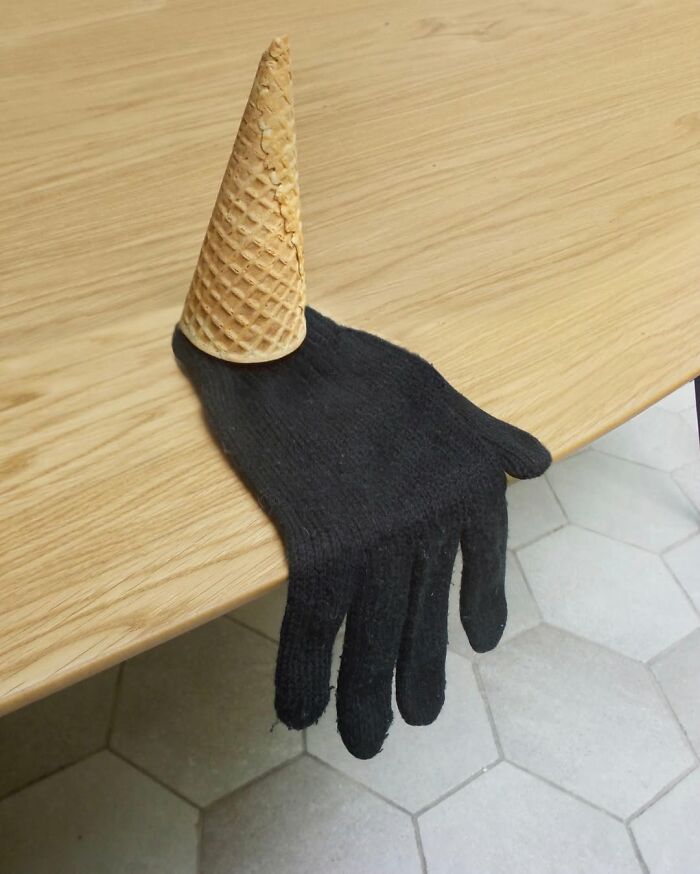 A black glove with an ice cream cone, creating an illusionary fusion on a wooden table.