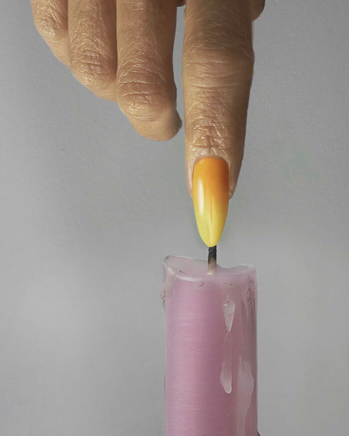 Finger illusion by Dudi Ben Simon, orange nail mimics candle flame on a pink candle, showcasing art of illusion.