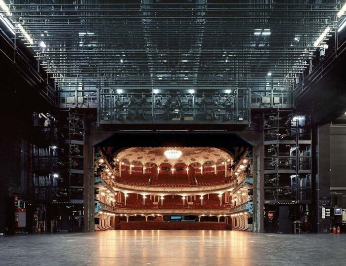 Backstage view of an iconic theater with ornate balconies, rich lighting, and a large chandelier.