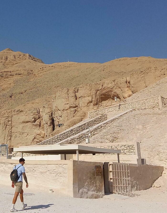 Man walking near iconic ancient site in a desert landscape under a clear blue sky.