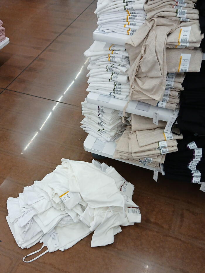 Clueless customer leaves clothes in a messy pile next to a neatly stacked shelf in a store.
