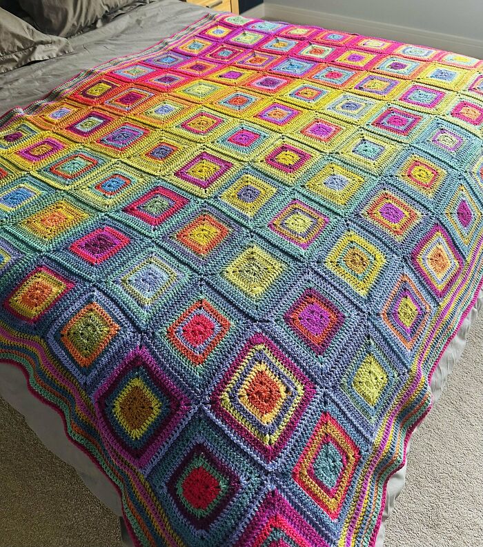 Colorful crochet blanket with intricate square patterns spread over a bed, showcasing incredible crochet craftsmanship.